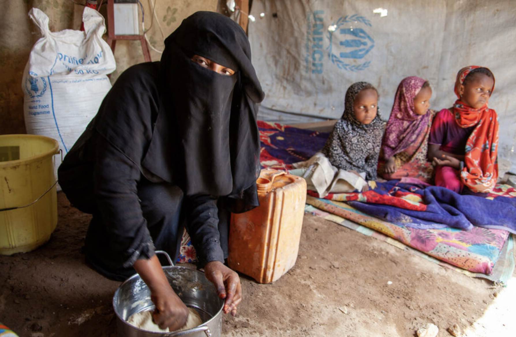 A woman prepares food for her three children in a Yemen settlement for displaced people