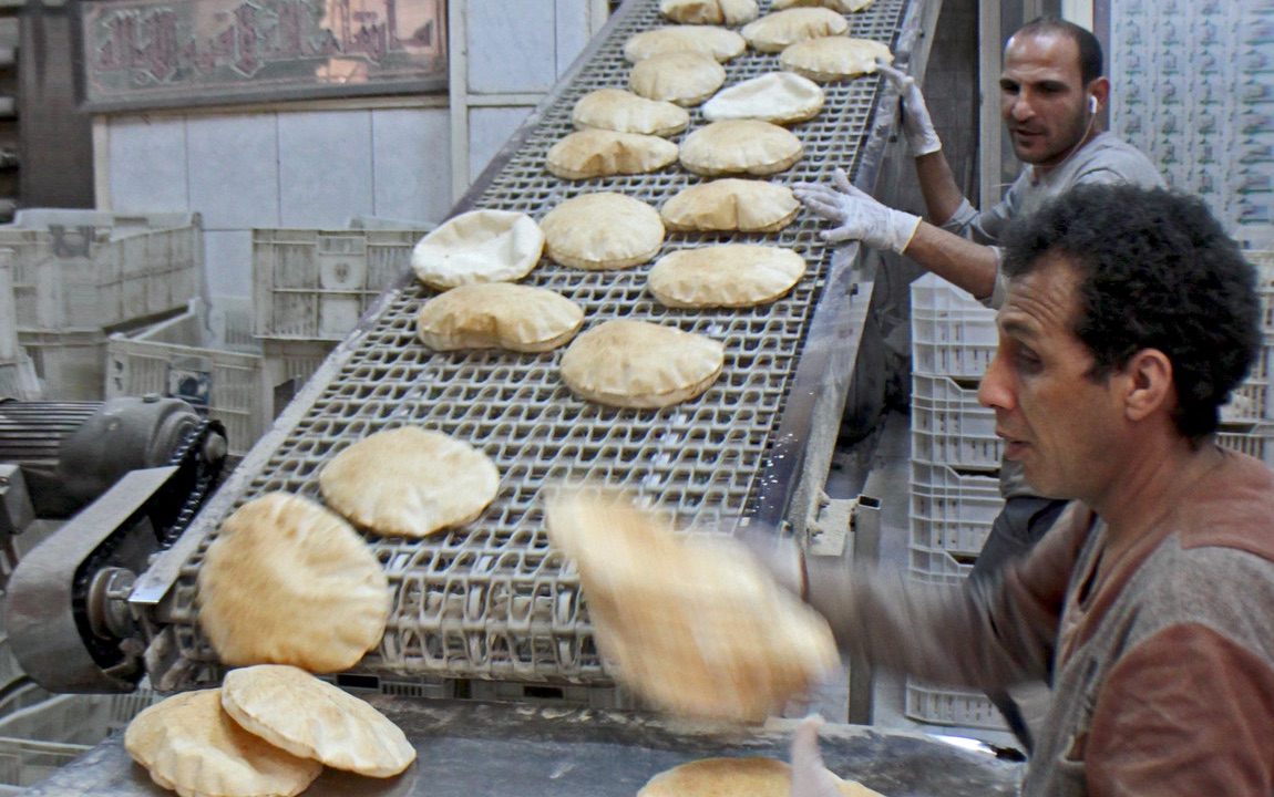 Two men next to conveyor belt with hot pita bread