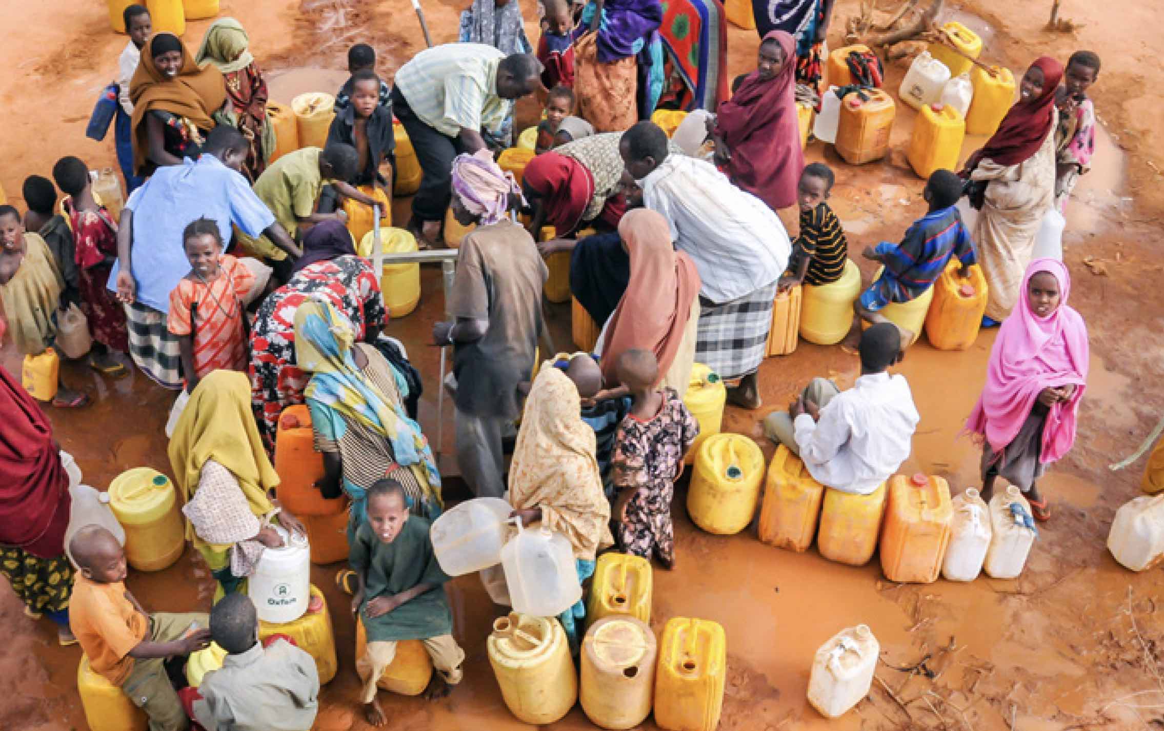 Overhead view of group of men, women, children gathering with water containers around spigots
