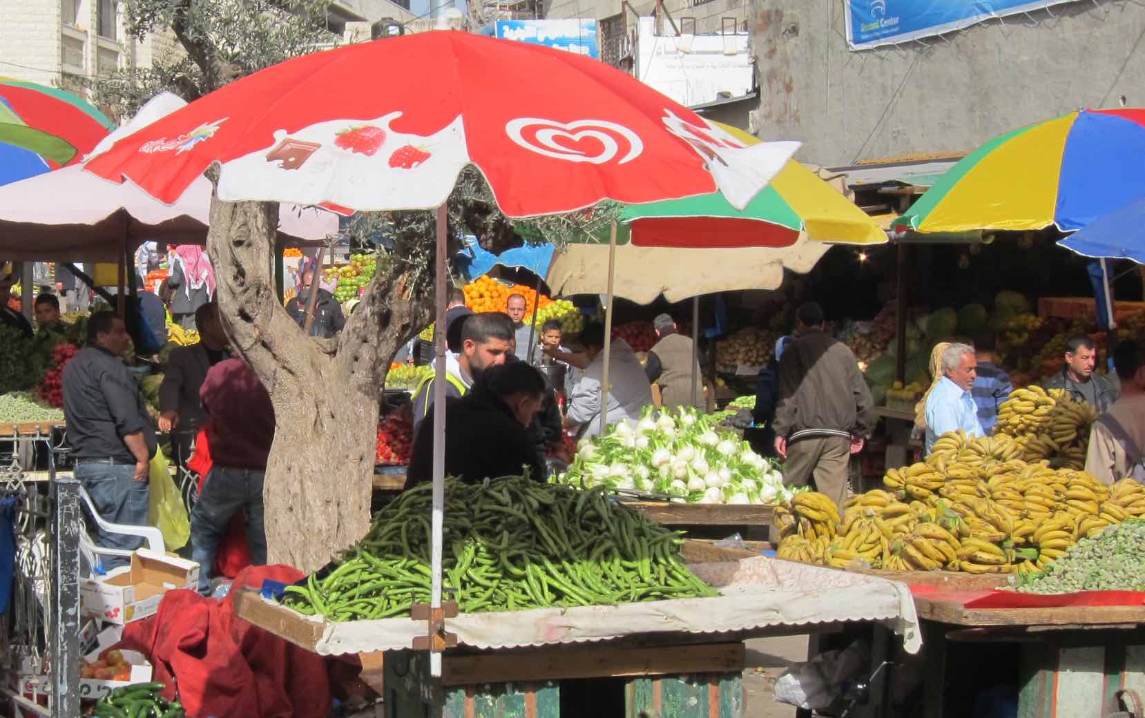 Fruits and vegetables on carts, one with a red umbrella, with people