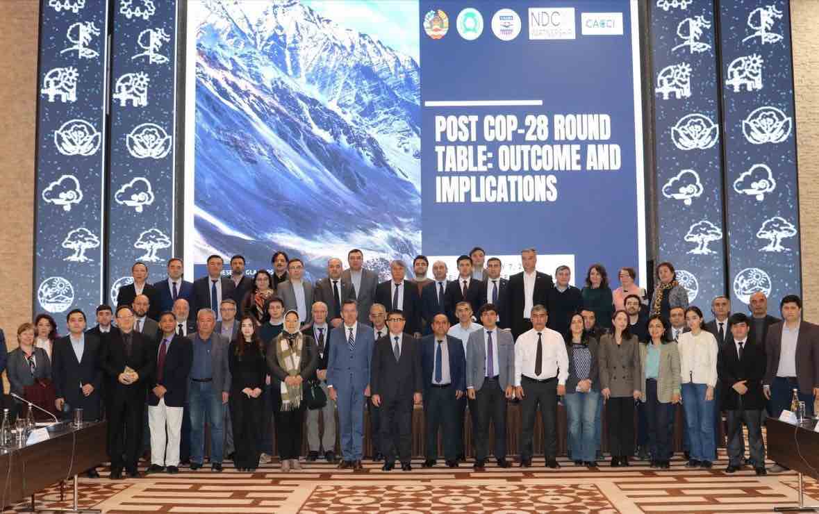 Large group of people in front of sign saying "Post COP28 Roundtable: Outcome and Implications
