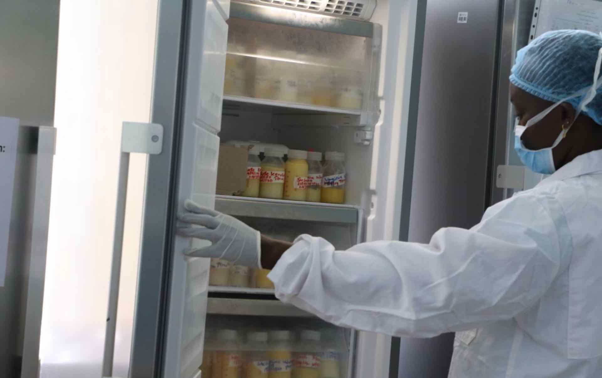Hospital worker with hand on open refrigerator door looks at bottles of donated human milk