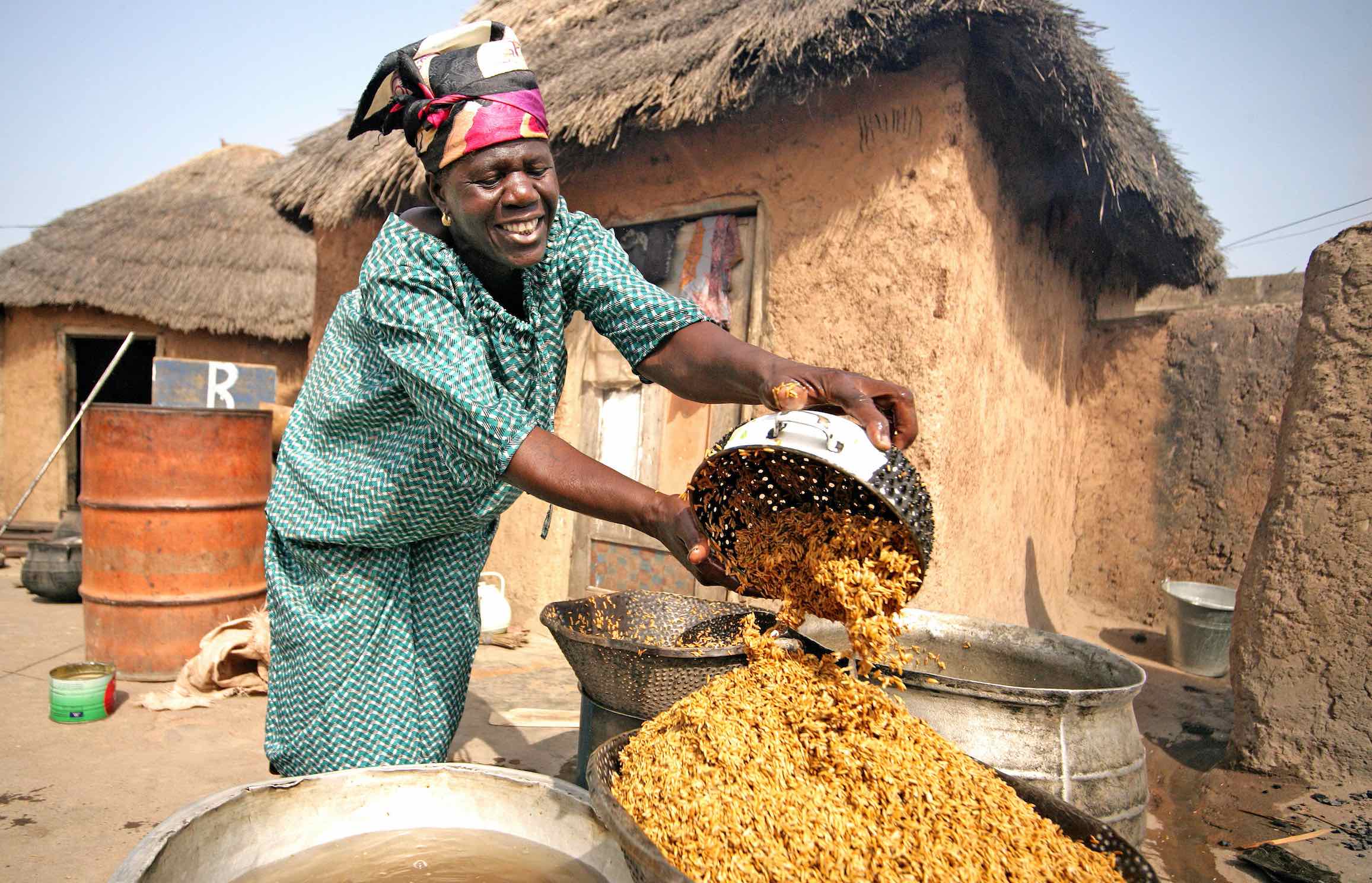 Woman sifts yellow rice from a bowl into a larger bowl with building in background